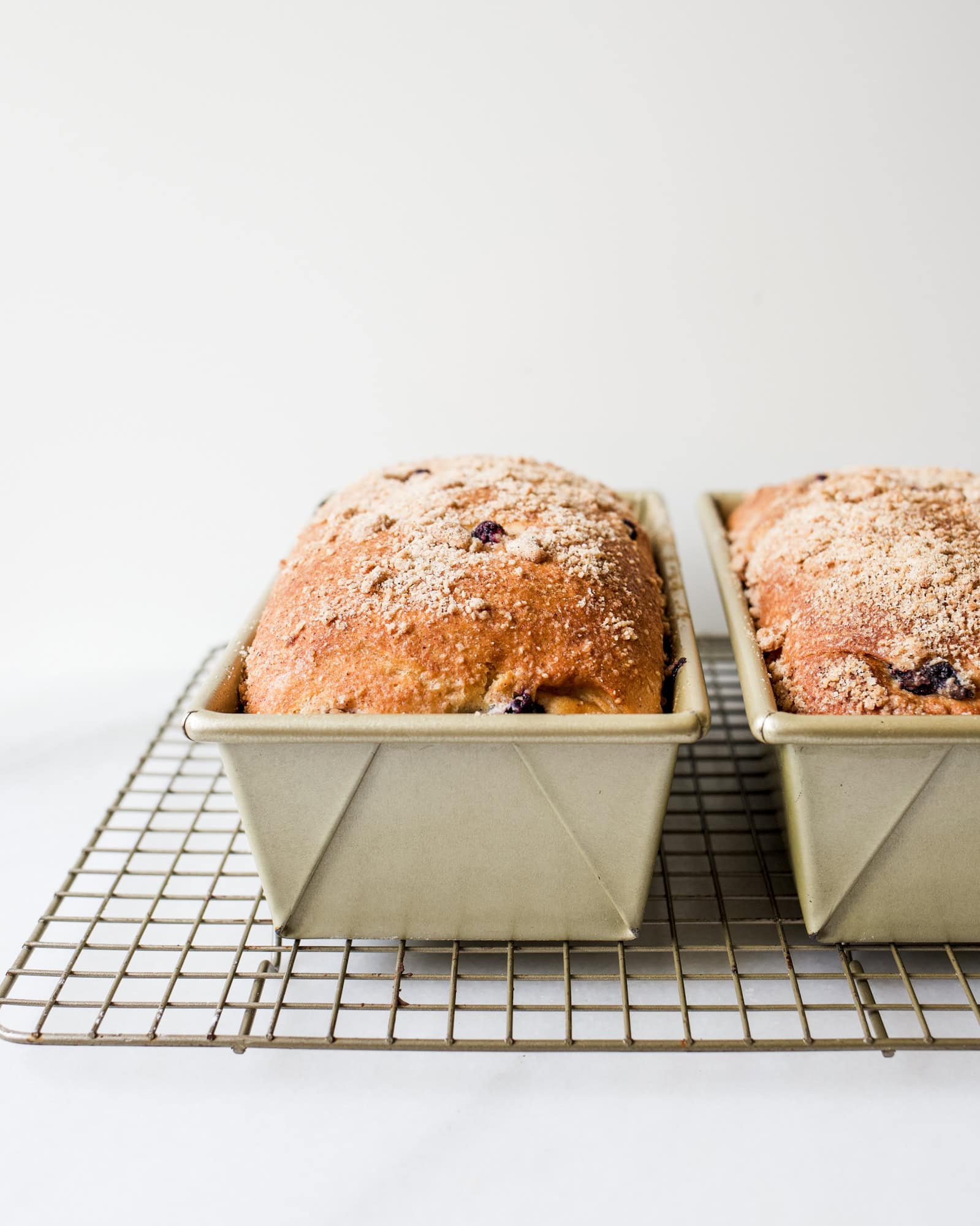 Blueberry Brioche recipe by Wood and Spoon blog. This is a recipe for two yeast loaves of brioche made with butter, egg, and a smidge of sugar. The fluffy white bread is studded with blueberries and seasoned with cinnamon. Each loaf has an optional crumble topping for extra sweet and salty in each bite. Learn how to fold and create this beautiful homemade breakfast treat here at thewoodandspoon.com by Kate Wood.